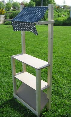 a wooden shelf sitting on top of a lush green grass covered field next to a blue and white umbrella