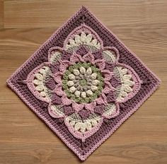 a crocheted square on a wooden floor with a pink and green flower design