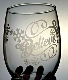 someone holding up a wine glass with the word believe etched in snowflakes on it