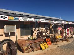 an old rusted out car sits in front of a store with signs on it