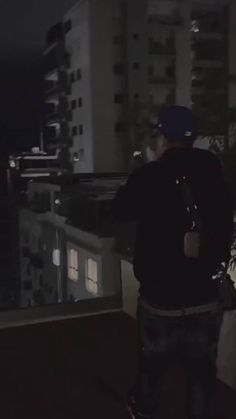 a man standing on top of a roof next to a tall building at night time