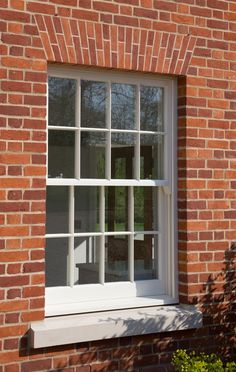 a brick building with an open window and white trim on the windowsill, in front of a tree