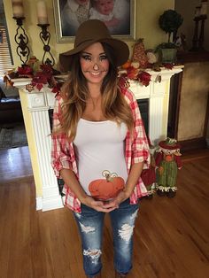 a pregnant woman standing in front of a fireplace with her belly exposed, wearing ripped jeans and a plaid shirt