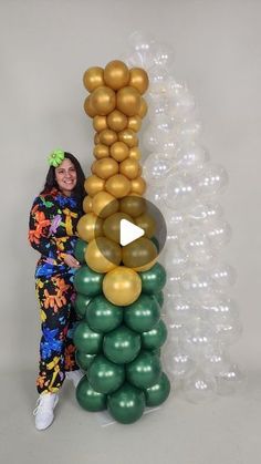 a woman standing next to a bunch of balloons in front of a white wall with gold and green balloons on it