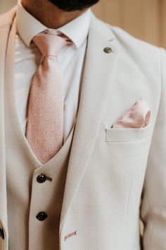 a man in a white suit with a pink tie and pocket square on his lapel