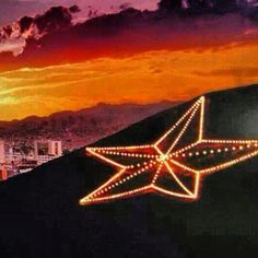 a lighted star on the side of a building at sunset with mountains in the background