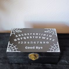 "Ouija Storage Box The box is painted black and has a brass clasp on it to help keep your items inside safe. The design on top is a white Ouija board with spider webs made out of vinyl. Inside the box you can choose rather you want it with velvet or without velvet.  You can use this box to store your jewelry, tarot cards or even your altar items.  Box measurements: 6\" x 4\" x 2.5\" Follow the link for more spooky fun items: https://www.etsy.com/shop/Nocturnalmporium If you have any questions about this item or would like a custom order please contact me. Be sure to follow me on Instagram: @nocturnalemporium" Diy Ouija Board, Altar Items, Halloween Boxes, Farmer Market, Senior Stuff, Christmas Money Holder, Cute Skeleton, Creepy Christmas, Trick R Treat