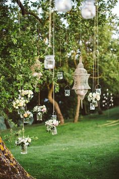 an outdoor wedding with hanging mason jars and floral centerpieces on the tree branches