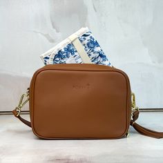 a brown cross body bag sitting on top of a white counter next to a blue and white towel