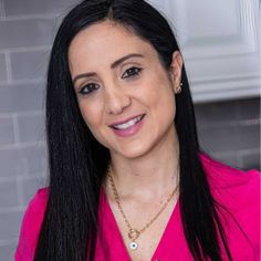 a woman with long black hair wearing a pink shirt and gold necklace smiling at the camera