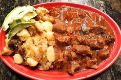 a red plate topped with meat, potatoes and avocado on top of a table