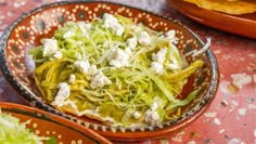 a bowl filled with lettuce and feta cheese on top of a table