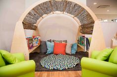 a living room filled with green couches next to a wooden arch and bookshelves