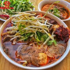 two bowls filled with meat and vegetables on top of a wooden table next to another bowl