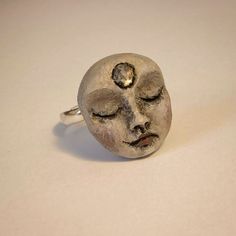 a silver ring with a face on it's side sitting on a white surface