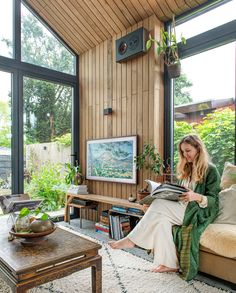 a woman sitting on a couch reading a book in her living room with large windows