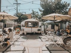 people sitting at tables with umbrellas and food trucks in the background