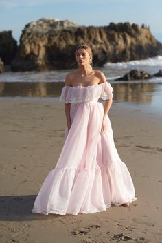 a woman standing on top of a beach next to the ocean wearing a pink dress