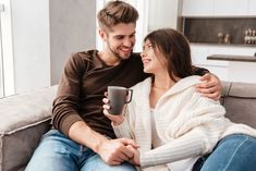 a man and woman are sitting on a couch holding coffee mugs in their hands