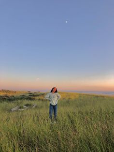 a woman standing in tall grass looking up at the sky