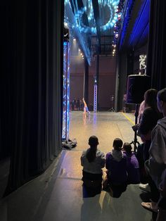 people sitting on the floor in front of a stage with blue lights and drapes