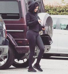 a woman in tights is looking at her cell phone while standing next to some cars