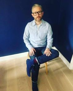 a man sitting on a chair in front of a blue wall with his legs crossed