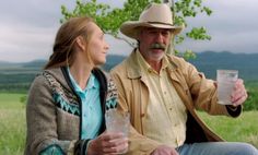 a man sitting next to a woman on top of a grass covered field holding a drink