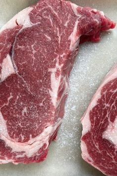 two raw steaks sitting on top of a counter next to each other in a bowl