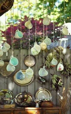 teacups hanging from the ceiling in front of a wooden wall with plates on it