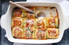 a casserole dish with cheese and spinach in it, next to a spoon