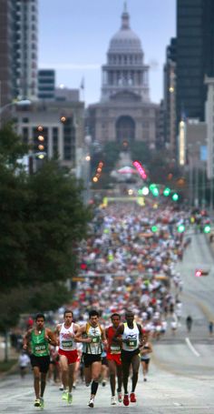 a large group of people running down a street with buildings in the backgroud