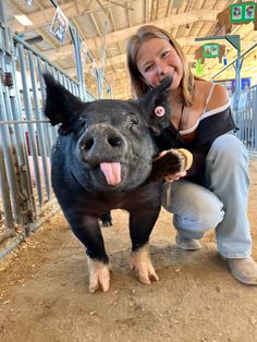 a woman kneeling down next to a pig with its mouth open and tongue hanging out