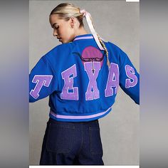 a woman wearing a blue jacket with the word texas printed on it and a ponytail in her hair