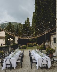 an outdoor dining area with tables and chairs, lights strung over the top of them