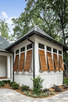 a small white building with wooden shutters on the front and side windows that are open