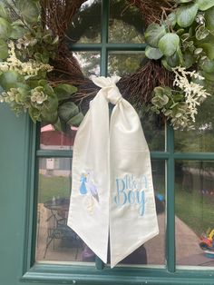 a wreath is hanging on the window sill in front of a green door with white flowers