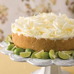 a cake with limes and white frosting on a silver platter next to a floral wallpaper