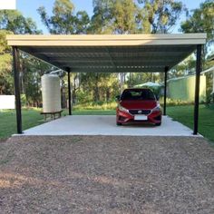 a red car is parked in the driveway under a metal carporture on gravel