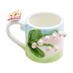 a ceramic mug with flowers and a butterfly on it's handle, sitting next to a white background