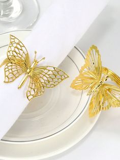 two gold butterflies sitting on top of a white plate next to a wine glass and napkin