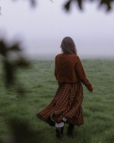 a woman in a long dress walking through a field on a foggy day with her back to the camera