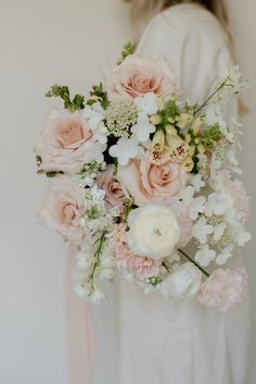 a woman holding a bouquet of pink and white flowers in her hands with the back of her body visible