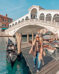 a woman standing on a dock next to gondola boats in venice, italy