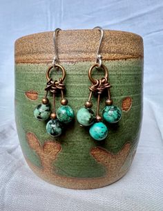 Rustic and boho earrings.  Three 5mm African turquoise stones hang on assymetrical copper wires. The African turquoise looks divine next to the copper. Very eye-catching.  These earrings hang on handmade sterling silver ear wires.  Very lightweight and versatile. African Turquoise, Rustic Jewelry, Turquoise Stones, Etsy Earrings Dangle, Earrings Boho, Copper Earrings, Gorgeous Earrings, Handmade Sterling Silver, Turquoise Stone