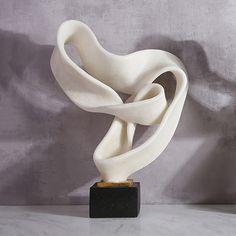 a white sculpture sitting on top of a marble table next to a gray wall,