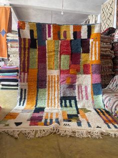 a multicolored rug with fringes on the floor in front of stacks of blankets