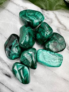 green and black marbles sitting on top of a white marble table next to a leaf