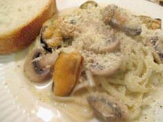 pasta with mushrooms and parmesan cheese on a plate next to a slice of bread