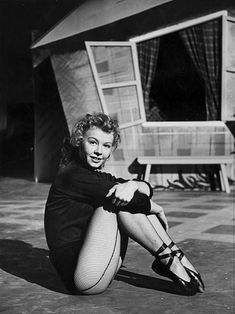 black and white photograph of a woman sitting on the ground in front of a house